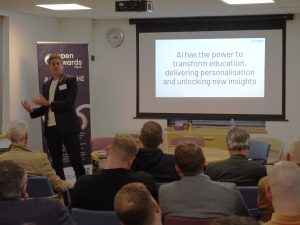 Kieron White of Engine AI stands at the front of a small conference room, delivering a presentation. A large projection screen behind him displays a slide that reads: "AI has the power to transform education, delivering personalisation and unlocking new insights."