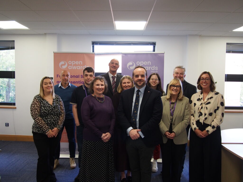 Open Awards staff and the Lord-Lieutenant of Merseyside pose for a group photograph at the Open Awards offices in Liverpool, in front of branded banners.